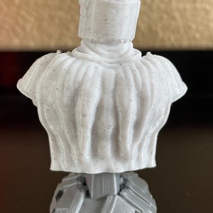 May include: A white 3D printed bust of a character wearing a helmet. The bust is on a gray base.