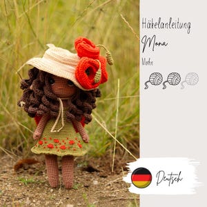 Op de afbeelding: Handgemaakte gehaakte pop met bruin haar, draagt een groene jurk met rode bloemaccenten en een strohoed versierd met rode klaprozen. De pop staat in een grasveld. Tekst op de afbeelding: "Häkelanleitung Mona Mohn".
