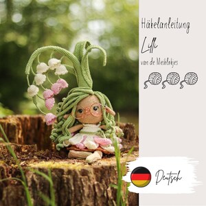 Könnte beinhalten: Häkelpuppe mit grünen Haaren und einer Maiglöckchenkrone, die ein weißes Kleid und eine Brille trägt. Die Puppe sitzt auf einem Baumstumpf. Das Bild enthält den Text "Häkelanleitung Lilli van de Meiklokjes Deutsch".