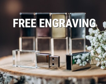 Könnte beinhalten: Nahaufnahme einer Kristall-USB-Stick mit einer silbernen Metallkappe. Der Stick liegt auf einer Holzoberfläche mit einem Strauß weißer Blumen im Hintergrund. Der Text "FREE ENGRAVING" ist auf dem Bild zu sehen.