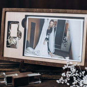 Peut inclure: Une boîte en bois avec un couvercle à charnières, contenant une photographie d'une femme en robe blanche. La boîte a une découpe pour une clé USB et est décorée de grain de bois.