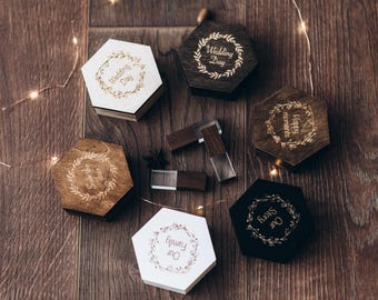 May include: Five hexagonal wooden boxes in white, natural wood, and dark brown finishes, each featuring a laser-engraved wreath and text including Wedding Day, Happy moments, Our Story, and Our Family, alongside two rectangular wooden USB drives.