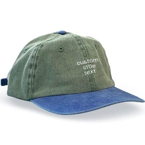 May include: A green and blue baseball cap with the text "custom little text" embroidered on the front.