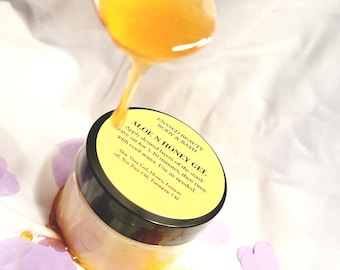 May include: A jar of Aloe N Honey Gel with a black lid, with a wooden spoon pouring honey. The jar is on a white surface with yellow powder and purple heart-shaped confetti. The label lists ingredients.