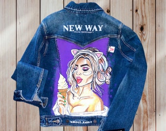 May include: A blue denim jacket with a painted design on the back. The design features a woman with cat ears, holding an ice cream cone. The text "NEW WAY - FOLLOW THE RABBIT -" is printed on the jacket. The text "FAMOUS_RABBIT" is printed on the bottom of the jacket.
