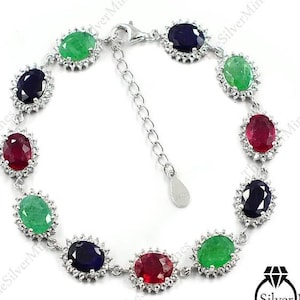 Può includere: Un bracciale in argento con una serie di pietre preziose dal taglio ovale in rosso, verde e blu scuro, ciascuna circondata da un alone di piccole pietre bianche. Il bracciale include un'estensione a catena in argento con una piccola targhetta.