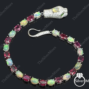 Puede incluir: Una pulsera de plata con ópalos y rubíes ovalados alternados. El cierre de la pulsera es de gancho y ojo. La cabeza de serpiente está incrustada con pequeñas piedras transparentes y tiene ojos verdes. Una joya única.