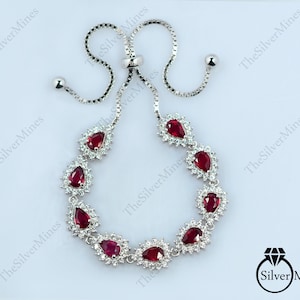 Può includere: Un bracciale bolo regolabile color argento con sette pietre preziose rosso scuro a forma di pera, ciascuna circondata da un alone di piccole pietre bianche trasparenti. Il bracciale ha una catena con due perline scorrevoli e il testo TheSilverMines.