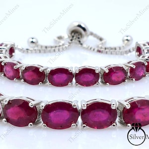 Könnte beinhalten: Ein silberfarbenes, verstellbares Bolo-Armband mit einer Reihe oval geschliffener, dunkelroter Edelsteine in Metallfassungen. Das Armband verfügt über einen Schiebemechanismus mit zwei kleinen silbernen Kugeln an den Kettenenden.