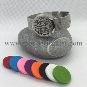Könnte beinhalten: Ein silbernes Edelstahlarmband mit einem runden Diffusor im Baum-des-Lebens-Design. Das Armband hat ein Mesh-Band und wird mit zehn Filzpads in verschiedenen Farben geliefert: Rot, Blau, Rosa, Lila, Orange, Schwarz, Weiß und Grün.