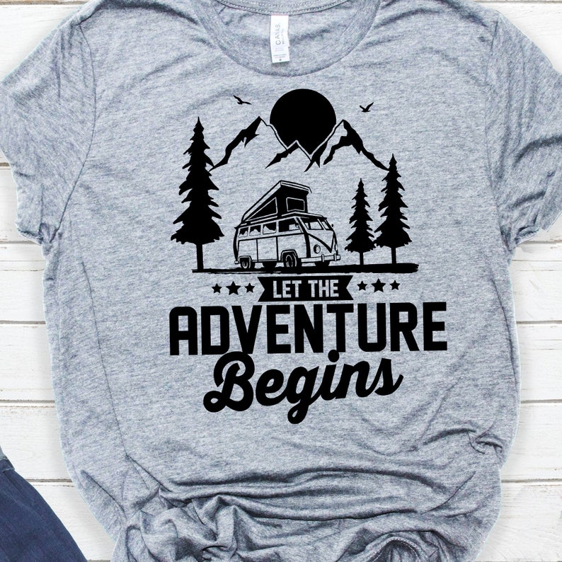 May include: Grey t-shirt with a black graphic of a camper van driving through a mountain landscape with a sun and trees. The text "Let the Adventure Begin" is below the camper van.