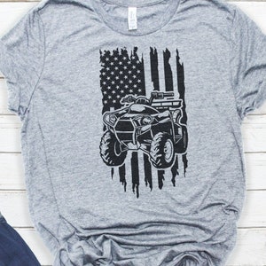May include: A gray t-shirt with a black and white American flag design featuring an ATV in the center.