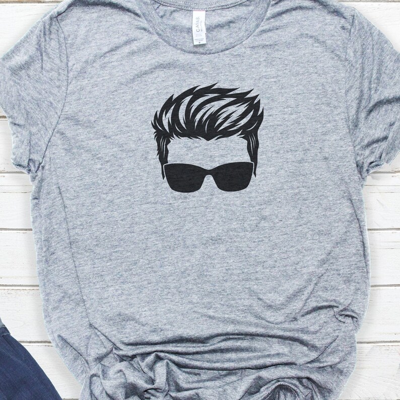 May include: A grey t-shirt with a black silhouette of a person wearing sunglasses.