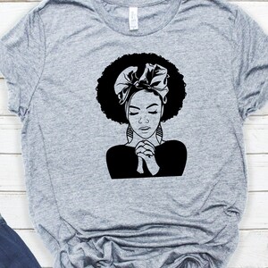 May include: Black and white illustration of a woman with an afro hairstyle wearing a headscarf and praying with her hands clasped together.