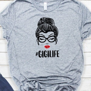 May include: Gray t-shirt with a black and white illustration of a woman with a bun, glasses, and red lips. The text "#GIGILIFE" is printed below the illustration.