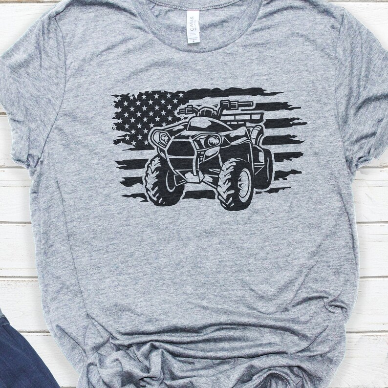 May include: A gray t-shirt with a black and white graphic of an ATV driving over a distressed American flag.