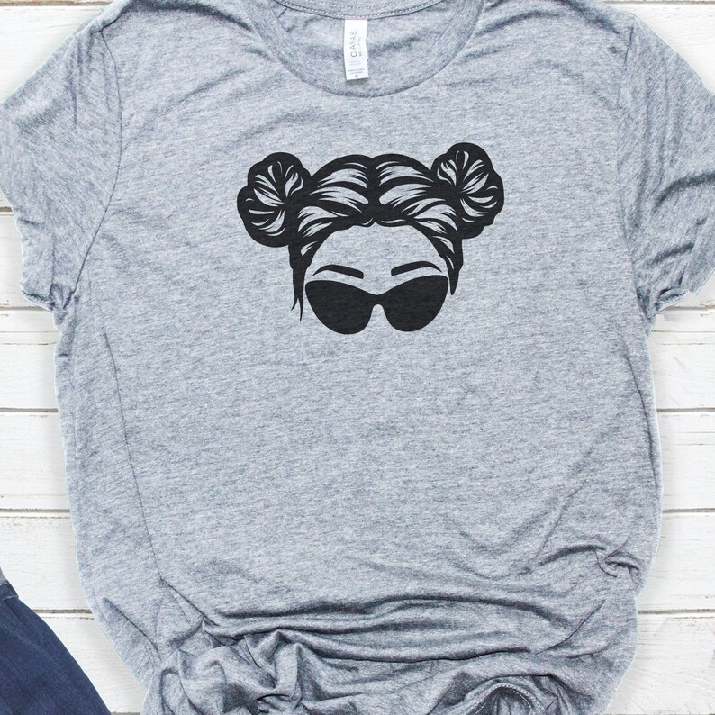 May include: A grey t-shirt with a black graphic of a woman with her hair in two buns and wearing sunglasses.