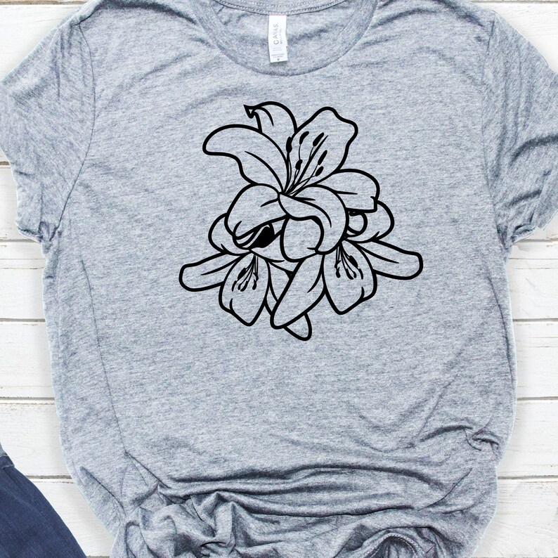 Puede incluir: Una camiseta gris con un dise&ntilde;o floral negro de lirios. El gr&aacute;fico es un contorno detallado de las flores, mostrando sus p&eacute;talos y estambres. La camiseta est&aacute; hecha de un material suave.