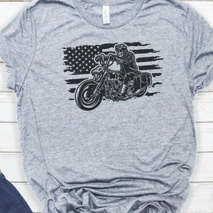 May include: A gray t-shirt with a black and white graphic of a motorcycle rider in front of an American flag.