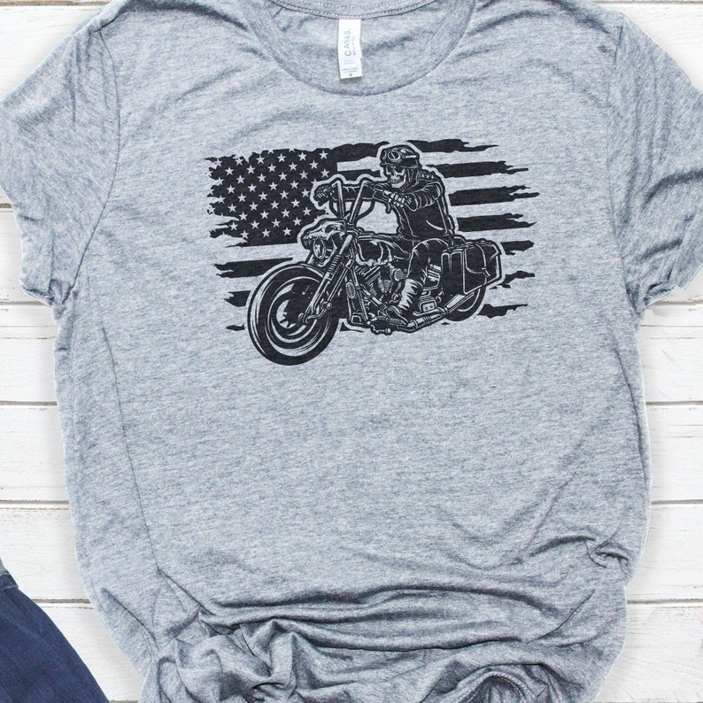 May include: A gray t-shirt with a black and white graphic of a motorcycle rider in front of an American flag.