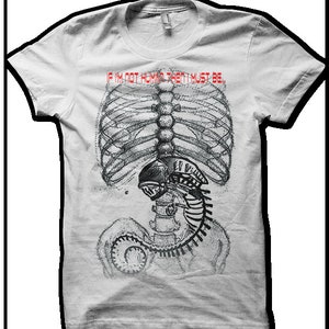 Puede incluir: Camiseta blanca con un estampado gr&aacute;fico de un esqueleto con una criatura alien&iacute;gena dentro de su caja tor&aacute;cica. El texto "If I'm not human then I must be..." est&aacute; impreso en rojo sobre el gr&aacute;fico.