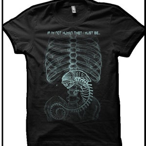 Puede incluir: Camiseta negra con un gr&aacute;fico de una imagen de rayos X de un torso humano con una criatura alien&iacute;gena en su interior. El texto "If I'm not human then I must be..." est&aacute; impreso sobre la imagen.