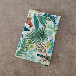 May include: A white fabric pouch with a tropical print featuring green leaves, orange and blue birds, and a white button closure.