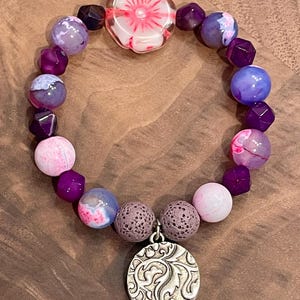 May include: A purple and pink beaded bracelet with a floral charm and lava rock beads.
