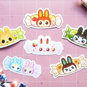 May include: Six colorful candy-themed stickers featuring cartoon bunnies with different expressions. Each sticker has a different color and design, with details like strawberries, apples, and candy wrappers.