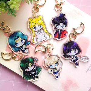 May include: Set of six anime character keychains featuring Sailor Moon characters. The keychains are made of clear acrylic and feature colorful illustrations of the characters. The keychains are attached to gold-colored metal rings.