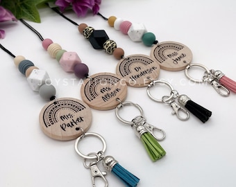 Puede incluir: Una colección de cordones para profesores con colgantes de arcoíris de madera y cuentas de colores. Cada cordón presenta un nombre diferente, como "Mrs. Parker" y "Dr. Henderson". Los cordones tienen llaveros plateados y borlas a juego en varios colores.