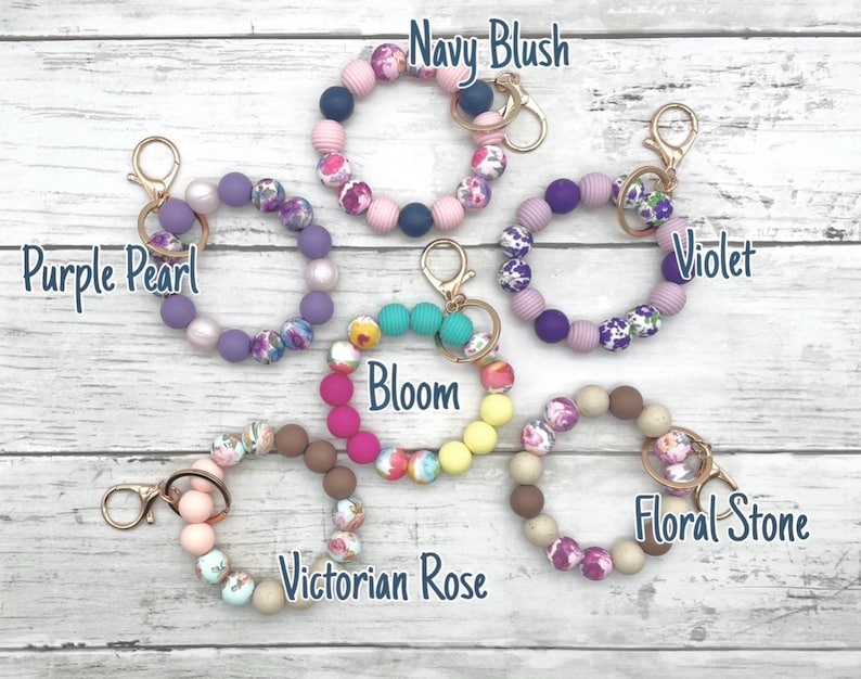 May include: Ten colorful silicone beaded keychains with floral patterns and gold key rings. The keychains are labeled with names like "Navy Blush", "Purple Pearl", "Violet", "Bloom", "Victorian Rose", and "Floral Stone".