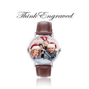 May include: A brown leather wristwatch with a silver face. The face of the watch has a photo of a family wearing Santa hats. The watch has the text "Think Engraved" above the watch.