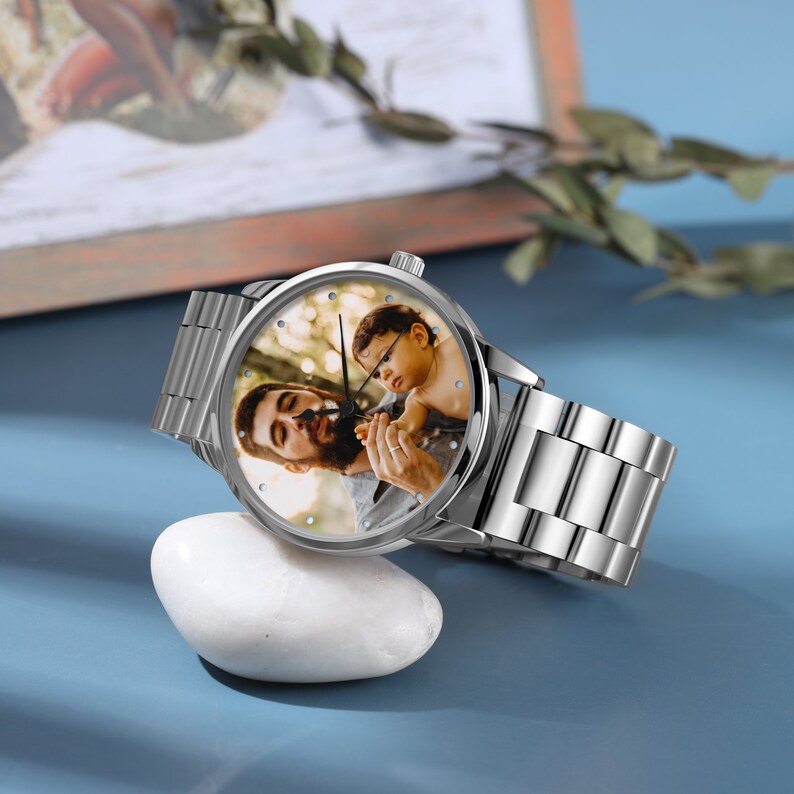 May include: A silver wristwatch with a round face featuring a photo of a man and a child. The watch has a silver metal band.