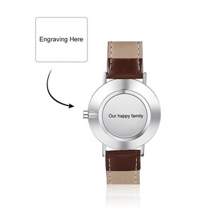 May include: A silver wristwatch with a brown leather band. The watch face is blank and has a space for engraving. The text "Our happy family" is engraved on the back of the watch.