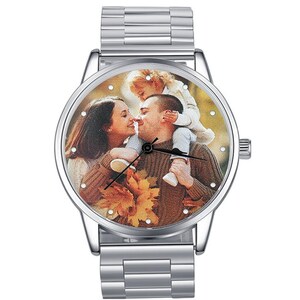 May include: A silver wristwatch with a round face and a photo of a family of three on the face. The photo shows a man and woman kissing with a child on the man's shoulders.