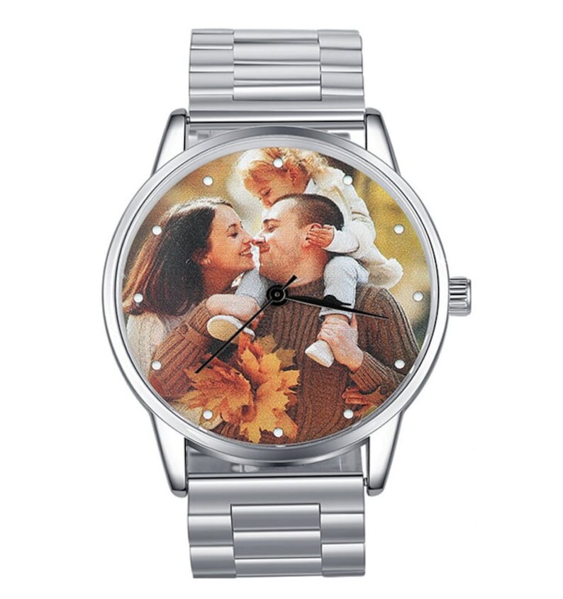 May include: A silver wristwatch with a round face and a photo of a family of three on the face. The photo shows a man and woman kissing with a child on the man's shoulders.