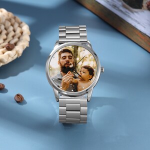 May include: A silver wristwatch with a round face featuring a photo of a man and a child. The watch has a silver metal band.
