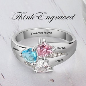 May include: A silver ring with three heart-shaped gemstones in blue, pink, and white. The ring is engraved with the names "Daisy", "Rachel", and "James", and the phrase "I love you forever". The text "Think Engraved" is above the ring.