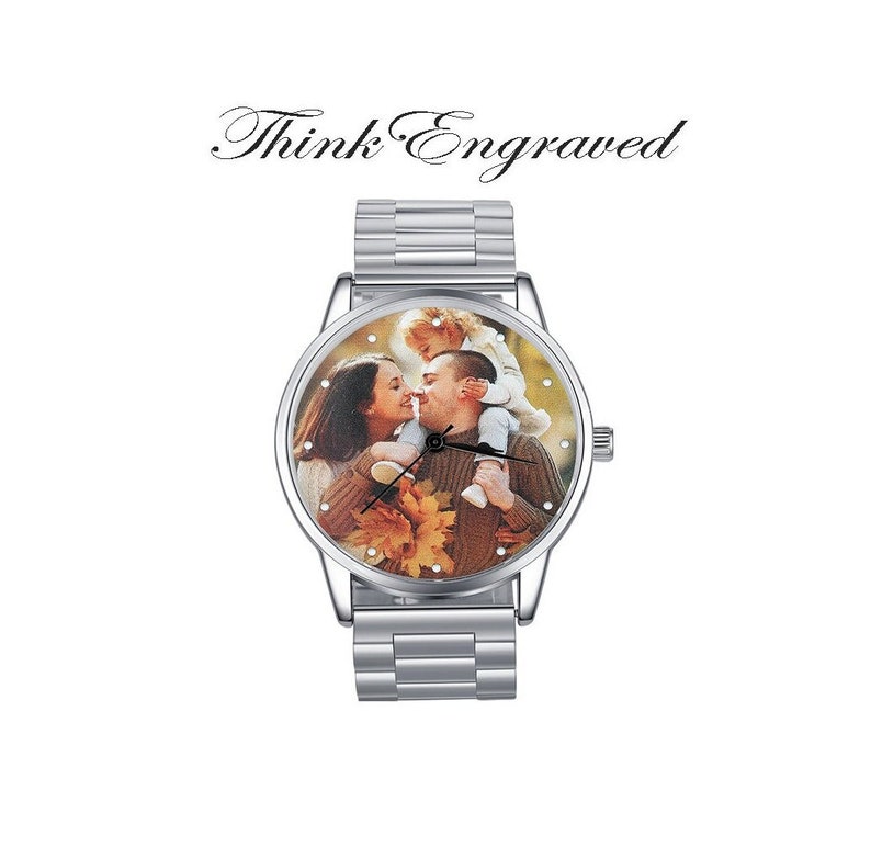 May include: A silver wristwatch with a round face featuring a photo of a family of three. The watch has a silver metal band.