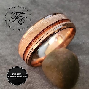 May include: A rose gold ring with a textured center band and dark brown inlays. The ring has a polished finish and is displayed with a small, rounded stone. The image includes the text "Free Engraving".