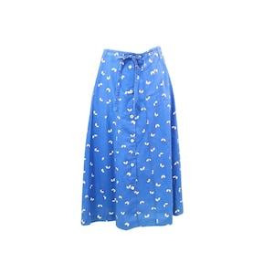 May include: A blue midi skirt featuring a repeating white and brown leaf-like pattern, a high-waisted design with a drawstring tie at the center, and a vertical row of white buttons running down the front of the garment from the waist to the hem.