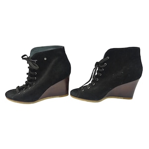 May include: A pair of black suede wedge ankle boots. The boots have a lace-up design and a wooden wedge heel. The boots are a dark black color and appear to be made of soft suede material. The wedge heel is approximately 3 inches high.