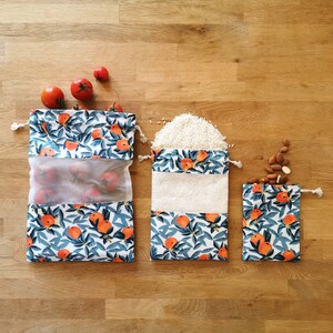 Peut inclure: Trois sacs à provisions réutilisables avec un fond blanc et un motif floral bleu et orange. Les sacs sont remplis de tomates, de riz et d'amandes.