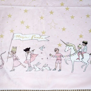 May include: A pink fabric with a gold star pattern and a whimsical illustration of a unicorn parade. The illustration features children, a unicorn, bunnies, and a banner that reads "Magic Parade".