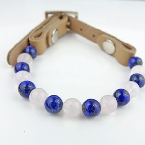 May include: A brown leather bracelet with blue and pink gemstone beads. The bracelet has a buckle closure.