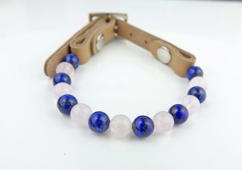 May include: A brown leather bracelet with blue and pink gemstone beads. The bracelet has a buckle closure.