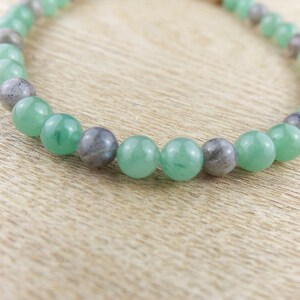 May include: A green and grey beaded bracelet with alternating round beads. The bracelet is made of natural stones.