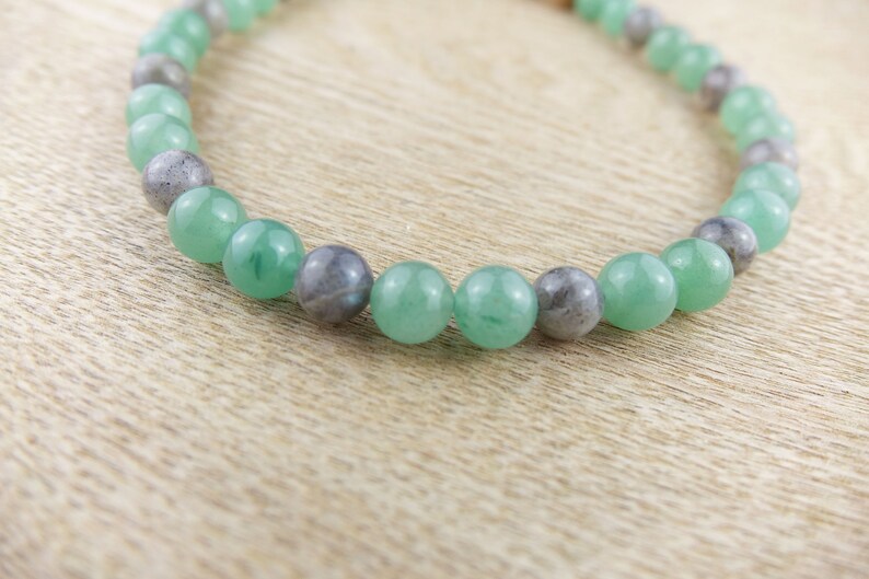 May include: A green and grey beaded bracelet with alternating round beads. The bracelet is made of natural stones.