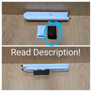 Könnte beinhalten: Ein weißer WLAN-Router mit einer schwarzen Montagehalterung. Der Router ist an einer Wand montiert. Die Halterung hat zwei Löcher für Schrauben.